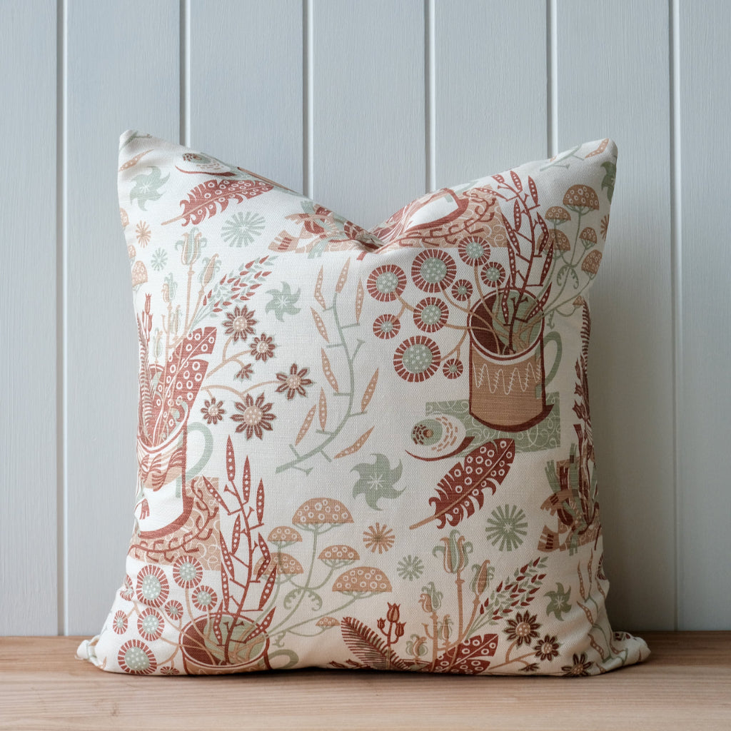 Decorative pillow with floral and nature-themed pattern on a wooden surface and light gray wall background