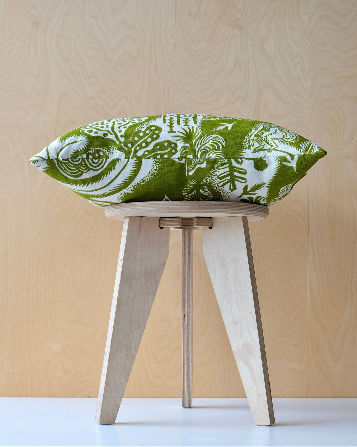 Wooden stool with a green and white patterned cushion on a light wooden background