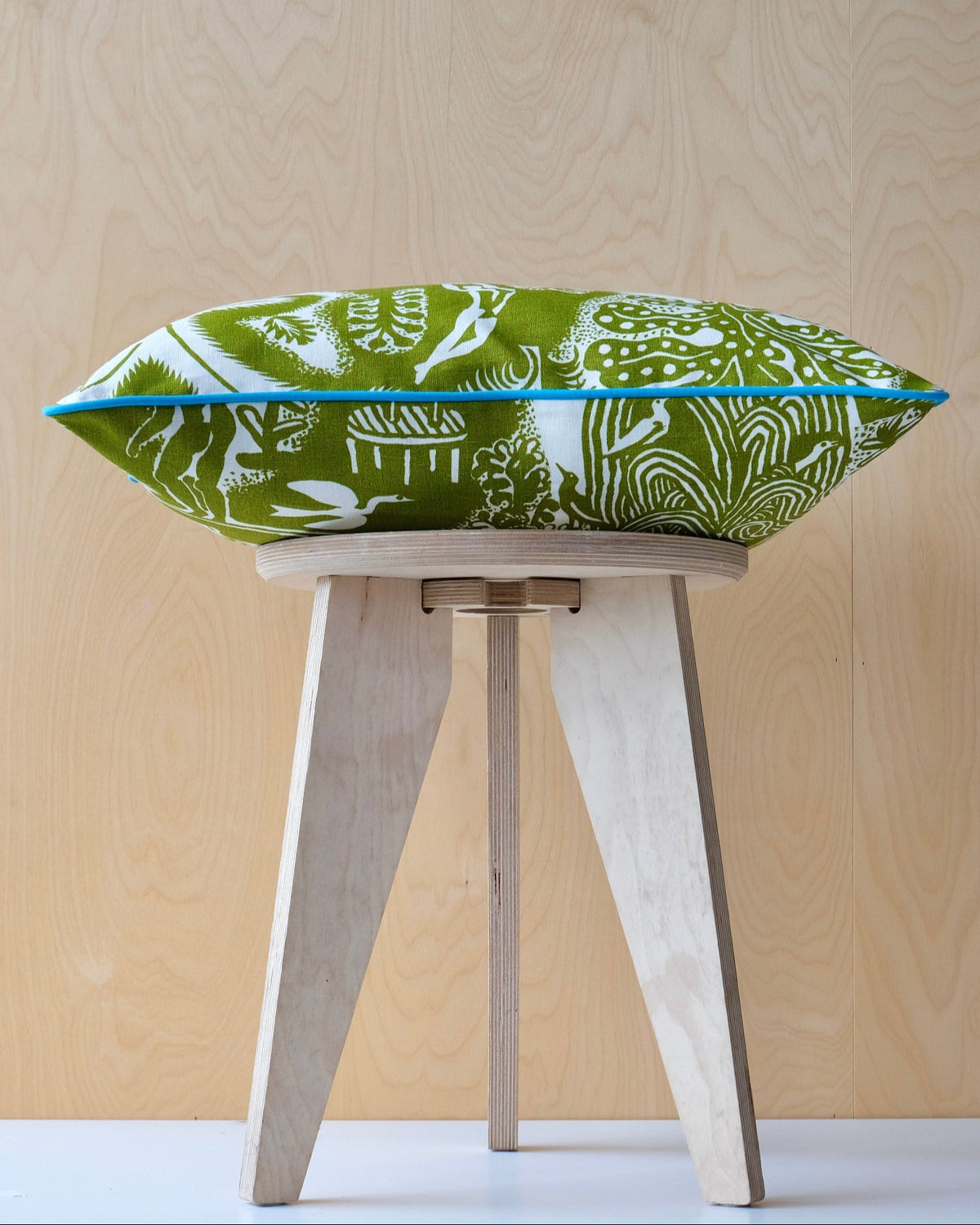 Green and white cushion with turquoise trim on a wooden stool with wood background
