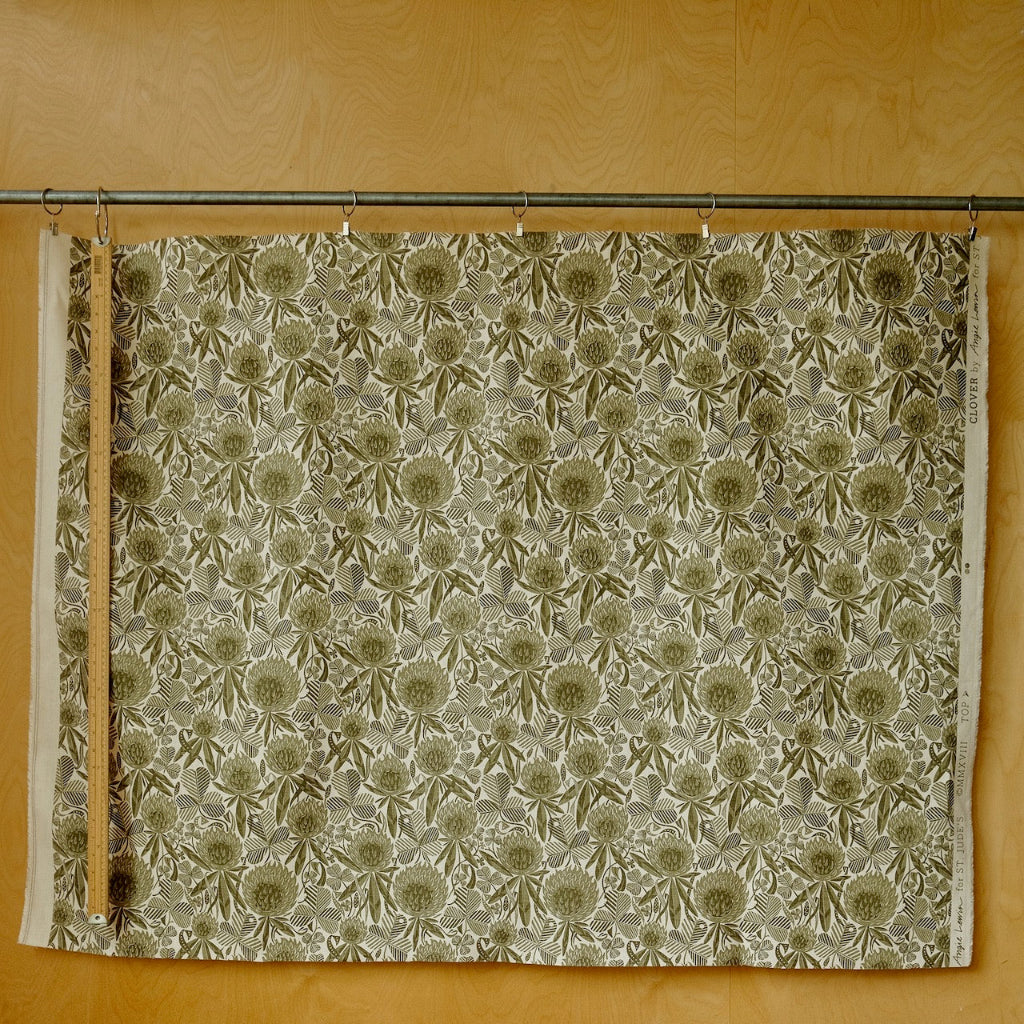 Green and white fabric with a floral pattern hanging on a rod against a yellow wall.