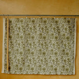 Green and white fabric with a floral pattern hanging on a rod against a yellow wall.