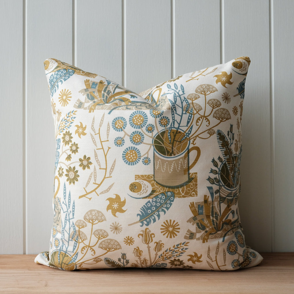 Decorative pillow with floral and nature-themed pattern on a wooden surface and light gray wall background