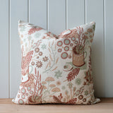 Decorative pillow with floral and nature-themed pattern on a wooden surface and light gray wall background