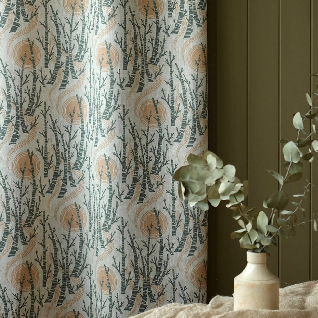 Curtain fabric with tree branch pattern next to a vase with greenery on a dark wall.