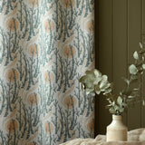 Curtain fabric with tree branch pattern next to a vase with greenery on a dark wall.