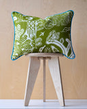 Green patterned cushion with turquoise piping on a wooden stool against a beige wall