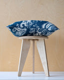 Blue and white patterned cushion on a wooden stool against a beige wall.