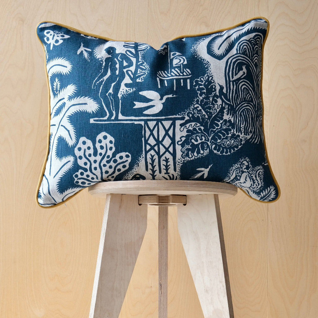 Decorative cushion with intricate blue design and ochre trim on a wooden stool against a beige background
