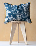 Decorative cushion with intricate blue design and ochre trim on a wooden stool against a beige background