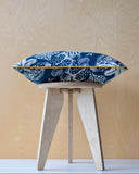 Blue patterned cushion with ochre trim on a wooden stool against a light wood panel background