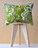Green patterned cushion with turquoise trim on a wooden stool against a light wood panel background
