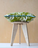 Printed fabric design of a cushion in green and white patterned fabric on a small wooden stool against a beige background
