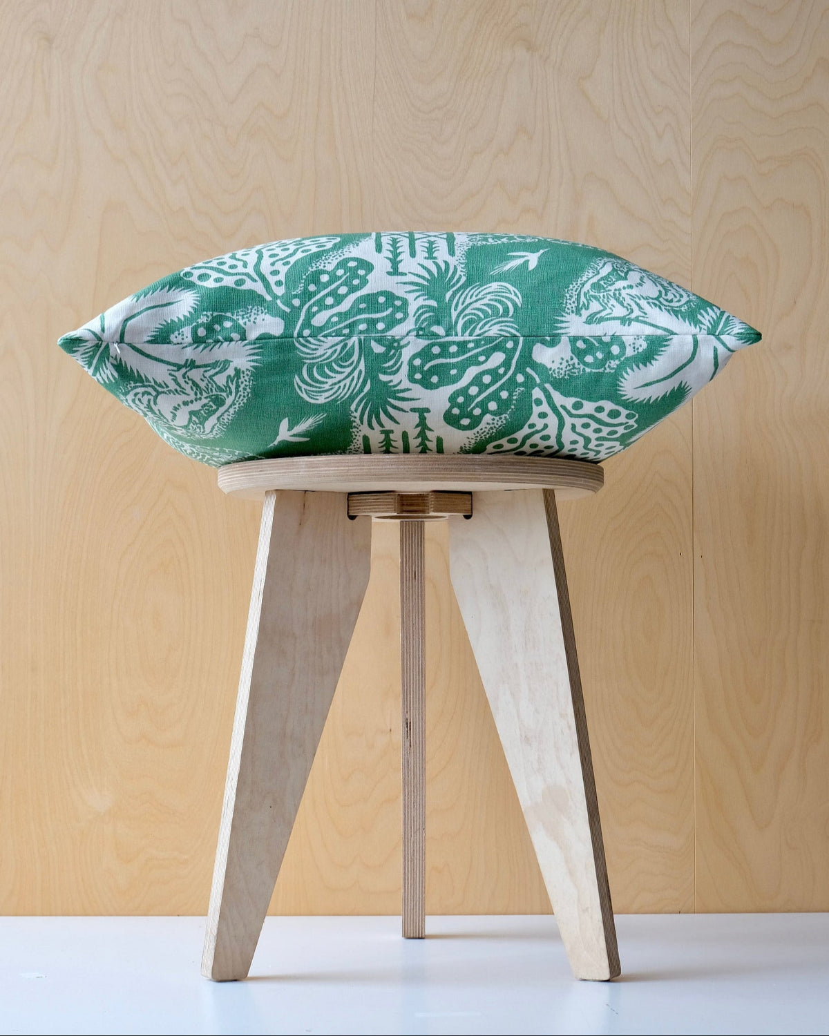 Green patterned cushion on a wooden stool with a ply background