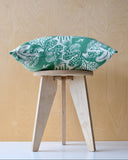 Green patterned cushion on a wooden stool with a ply background