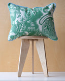 Decorative cushion with green and white pattern and pale blue trim on a wooden stool against a wooden background