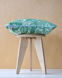 Green patterned cushion on it's side on a wooden stool against a light wood panel background