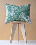 Decorative cushion with a green pattern and pink trim on a wooden stool against a beige background