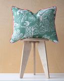 Decorative cushion with a green and white pattern on a wooden stool against a beige background