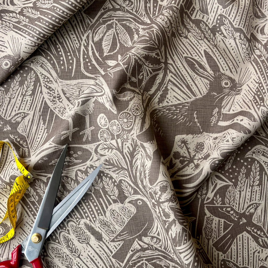 Brown fabric with hare and foliage pattern, scissors, and measuring tape on a matching fabric background