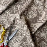 Brown fabric with hare and foliage pattern, scissors, and measuring tape on a matching fabric background