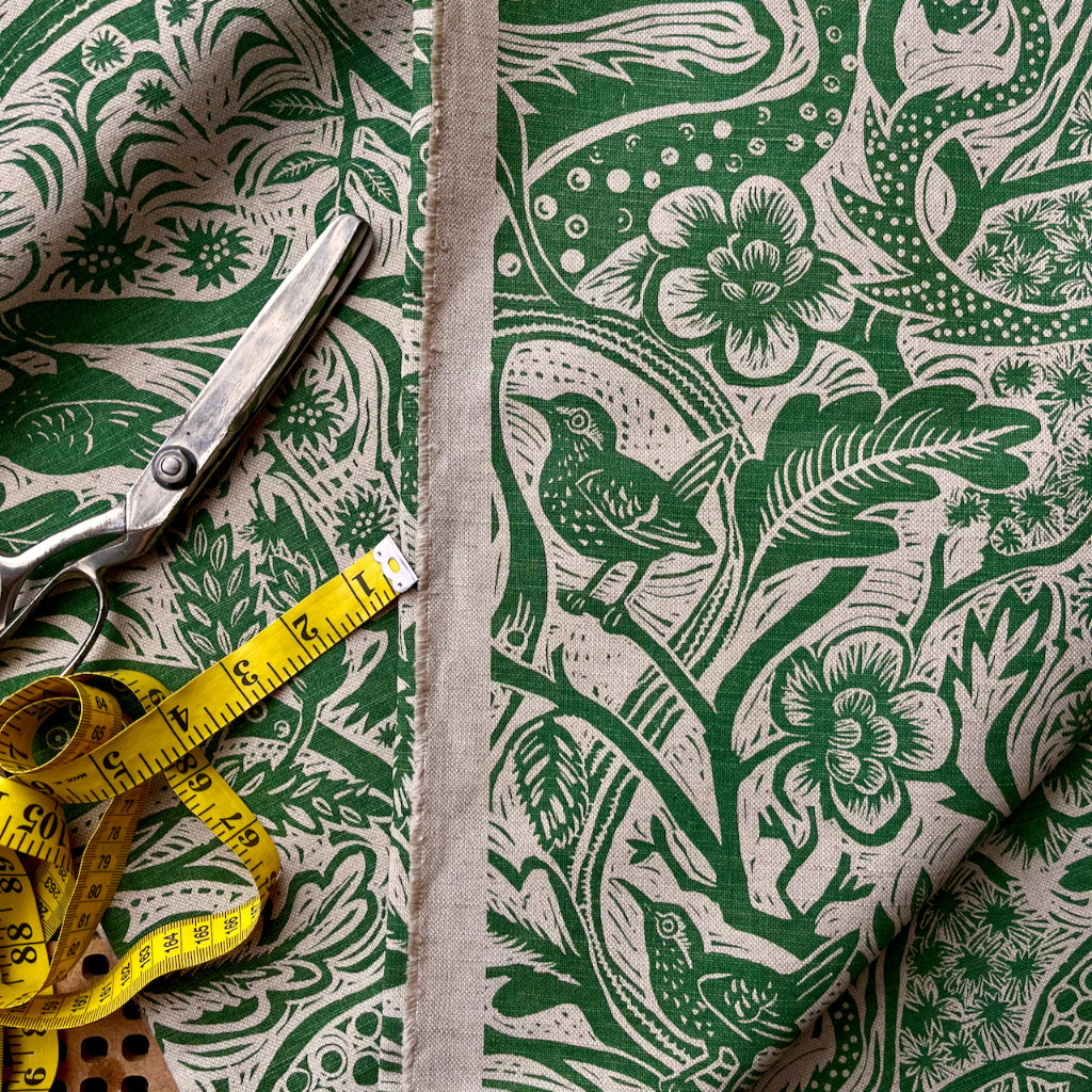 Fabric with green floral and bird pattern, scissors, and measuring tape on a matching fabric background.