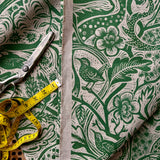 Fabric with green floral and bird pattern, scissors, and measuring tape on a matching fabric background.
